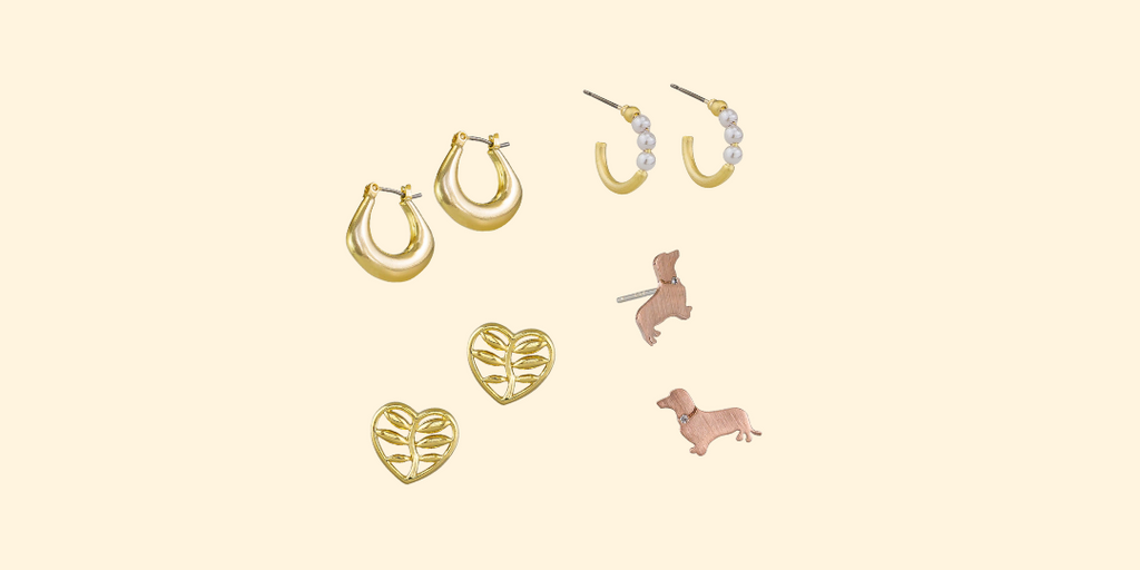 Four earrings on a cream background. Two pairs of gold hoops one has pearls. One pair of rose gold dog earrings and one pair of gold heart studs