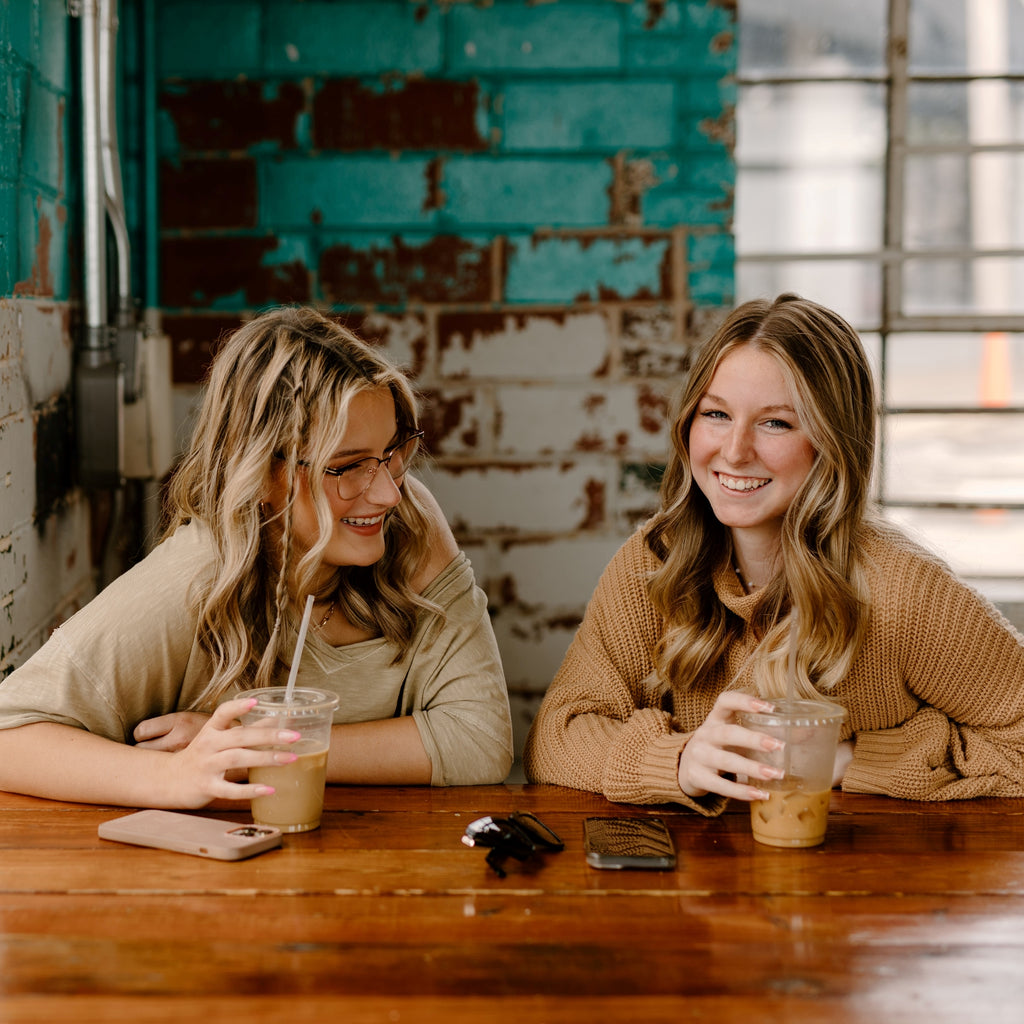 Two female friends drinking iced coffee and laughing in a cafe