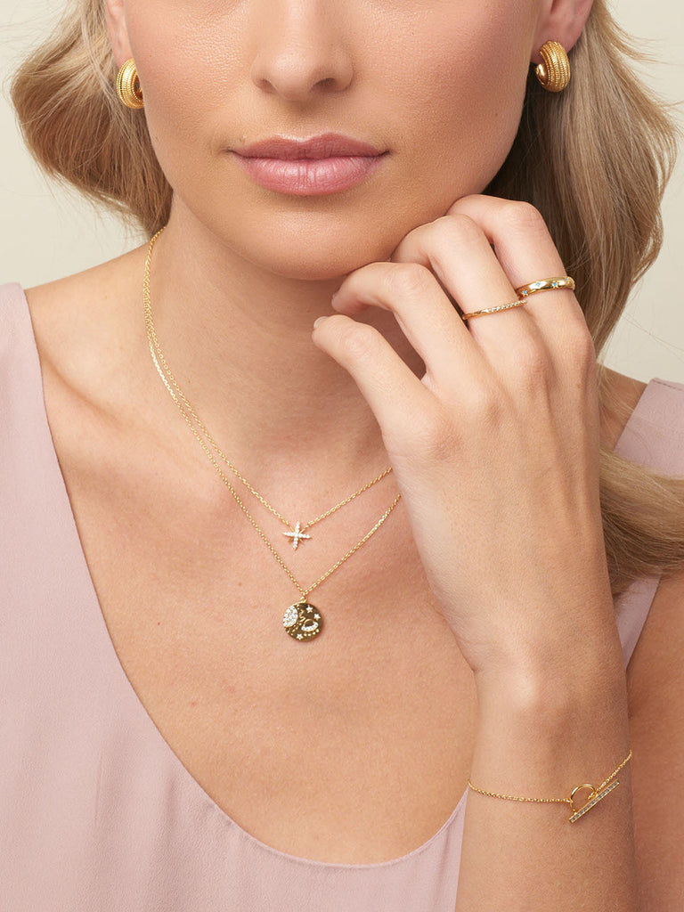 Blonde model wearing the gold My Lucky Star Necklace and a gold necklace with a gold disc pendant. Also wearing two minimalist gold rings