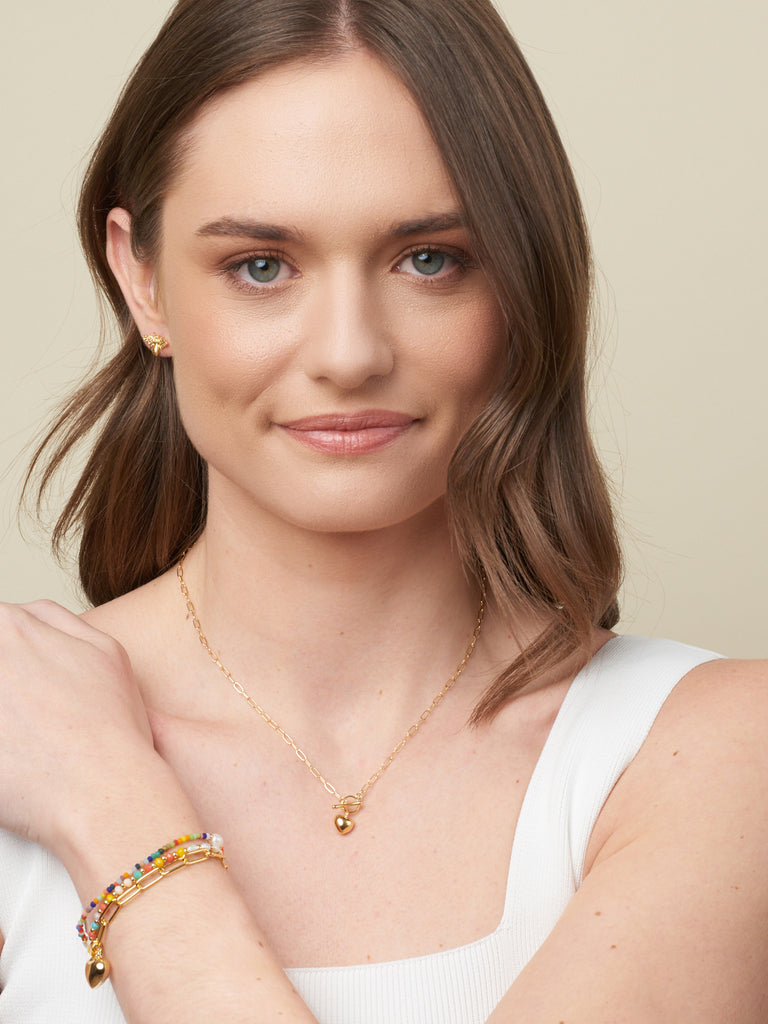 model with brown hair displaying gold necklace with fob and gold heart