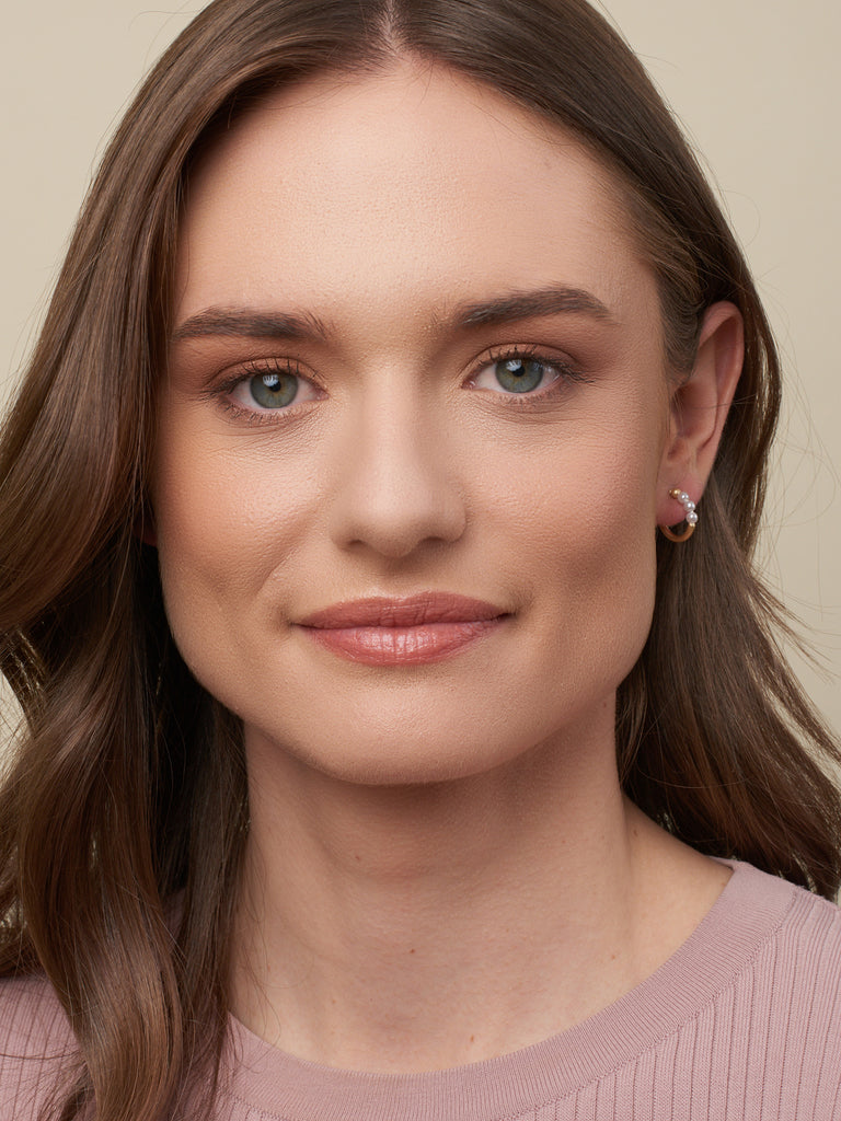 model with brown hair displaying coastal pearl huggies (semi-circle gold pearl hoops)